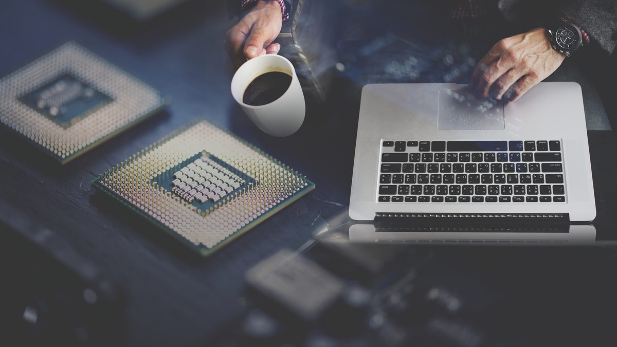 Departamento de Soporte IT interno. Un hombre con una Macbook y una taza de café resuelve problemas de tecnología sobre lo que parece ser una placa de circuitos.